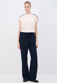 Blusa crema con dettaglio testurizzato sulle spalle, abbinata a pantaloni navy larghi con cintura elastica e pieghe morbide.
