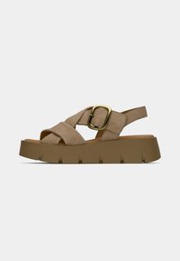 Suede sandals with a crossover strap design, a gold buckle detail, and a thick, textured brown platform sole.