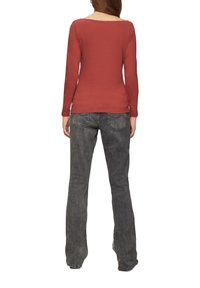 Lange mouwen roestkleurig top met een ronde hals, gecombineerd met grijze flared jeans met achterzakken en een vervaagde textuur.