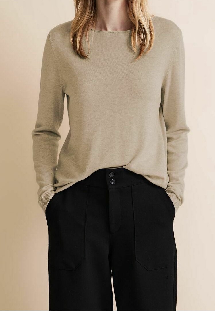 Light beige long-sleeve sweater with a rounded neck, paired with high-waisted black trousers featuring two front pockets and button closure.