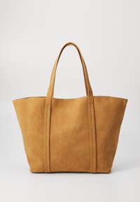 Grand sac fourre-tout beige fabriqué en matériau doux, avec deux anses plates et des détails cousus le long des côtés. Design à ouverture supérieure.