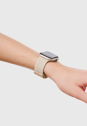 Smartwatch med et beige vævet bånd båret på et håndled mod en ensartet lys grå baggrund.