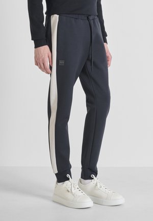 Marine joggers met een witte zijstreep, gemaakt van zachte stof. Heeft een elastische tailleband met trekkoord en een logo patch aan de voorkant. Gecombineerd met witte sneakers.