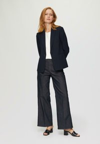 Marineblazer mit strukturierten Revers über einem weißen Hemd, kombiniert mit weit geschnittenen, dunklen Jeans und schwarzen Sandalen mit Absatz. Einfaches und maßgeschneidertes Design.