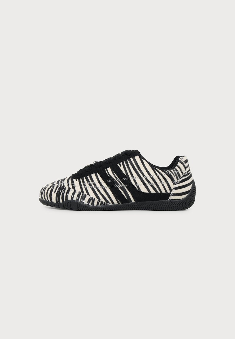 Baskets à lacets noires et blanches avec motif rayures zèbre et semelle noire texturée sur un fond clair uni.