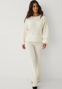 Cremfarbener Pullover und passende Hose aus weichem Strickstoff. Der Pullover verfügt über dezente Verzierungen am Ausschnitt. Lockere Passform.