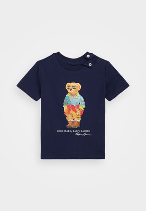 Granatowy bawełniany t-shirt z nadrukiem kreskówkowego misia w okularach przeciwsłonecznych i casualowym ubraniu, z guzikiem na ramieniu i nadrukowanym logo poniżej.