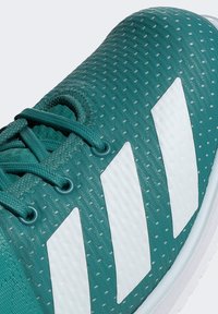 Tyrkysová atletická obuv s textúrovaným povrchom, tromi bielymi pruhmi a tyrkysovými šnúrkami. Obsahuje perforácie pre priedušnosť a hladkú podrážku.