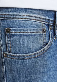 Blue denim jeans featuring a back pocket with metal rivets, contrast stitching, and a slightly faded texture.