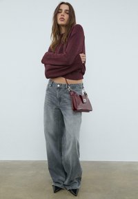 Burgunderfarvet strikket sweater, højttaljede falmede grå jeans, sorte spidse hæle og en lille burgunderfarvet håndtaske med en sølv spænde detalje.
