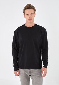 Svart långärmad t-shirt i bomull, rund halsringning, manschetter på ärmarna, kombinerad med ljusgrå jeans. Enfärgad design, utan mönster eller detaljer.