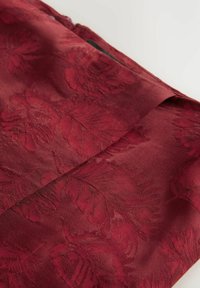 Tessuto bordeaux con un motivo floreale testurizzato, finitura liscia con un delicato lucido, pieghe visibili lungo i bordi e cuciture ordinate.