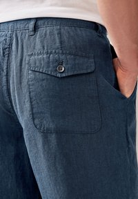 I pantaloni in lino blu scuro presentano una tasca posteriore con bottone, vestibilità sartoriale e un tessuto testurizzato per comfort e traspirabilità.
