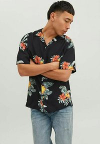 Maglietta nera a maniche corte con motivo di fiori e foglie tropicali in rosso, arancione e verde. Taglio dritto, colletto a bottoni, tessuto leggero.