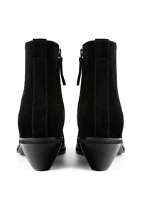 Cizme negre din suede, lungi până la gleznă, cu vârf ascuțit și toc geometric, având cusături decorative și un fermoar pe lateral pentru închidere.