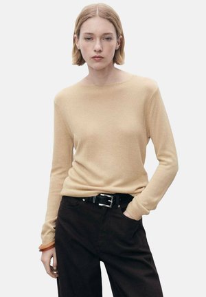 Beige ribbed knit sweater with long sleeves and a boat neckline, paired with dark brown pants and a black belt. Smooth texture, fitted design.