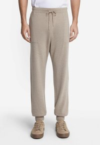 Jasno beżowe spodnie dresowe z miękkiego materiału, z elastycznym pasem ze sznurkiem, ściągaczami u dołu oraz bocznymi kieszeniami. Połączone z beżowymi butami na sznurówki.