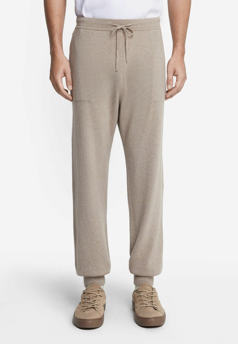 Jasno beżowe spodnie dresowe z miękkiego materiału, z elastycznym pasem ze sznurkiem, ściągaczami u dołu oraz bocznymi kieszeniami. Połączone z beżowymi butami na sznurówki.