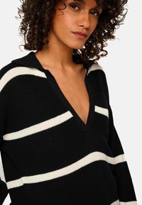 Pull-over rayé noir et blanc avec un col en V, manches longues, texture côtelée et design à col.