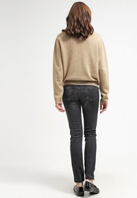 Suéter beige con puños y dobladillo acanalados, combinado con jeans ajustados negros y zapatos negros, visto desde atrás sobre un fondo claro.