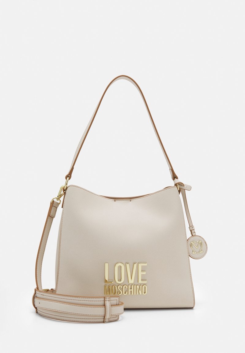 Sac à main beige Love Moschino avec logo doré, poignée supérieure unique, bandoulière amovible et breloque ronde de marque sur fond blanc.