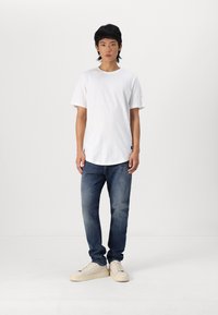 Camiseta de algodón blanca con mangas cortas, combinada con unos jeans azules y zapatillas color crema. Diseño sencillo, corte relajado y minimalismo en la marca.