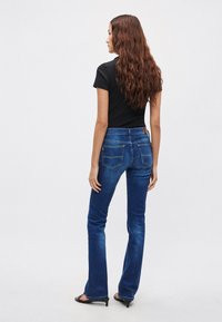 Ciemnoniebieskie dzwony jeansowe o gładkiej fakturze, z talią średniego wzrostu i tylnymi kieszeniami. Połączone z dopasowanym czarnym t-shirtem.