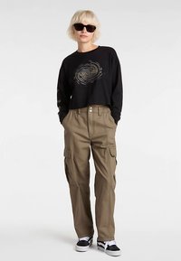 Maglietta nera a maniche lunghe corta con un logo circolare abbinata a pantaloni cargo beige con molte tasche e una vestibilità comoda.