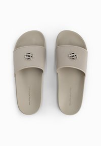 Lichtbeige slide sandalen met een brede band en een getextureerde logoaccent. De zool is plat met een matte afwerking.