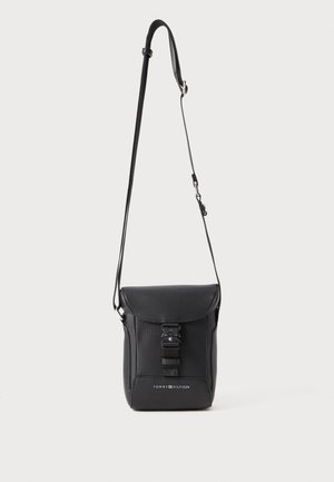 Black leather crossbody bag with a flap top, adjustable strap, snap closure, and embossed logo at the bottom. Smooth texture, rectangular shape.