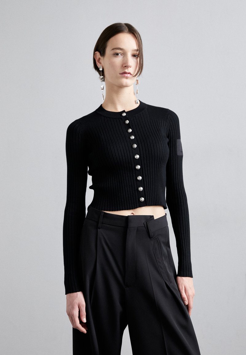 Zwarte geribbelde cropped cardigan met lange mouwen en parelachtige knopen aan de voorkant, gecombineerd met hooggetailleerde zwarte broek.