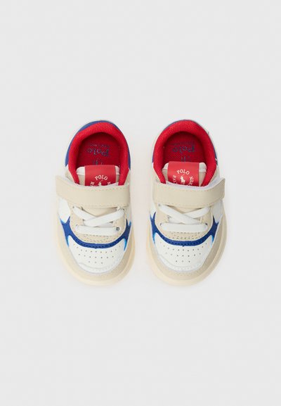 Zapatillas blancas y beige con acentos azules, correa de Velcro y forro interior rojo. Punta redondeada y parte delantera perforada para transpirabilidad.