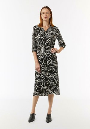 Zwart-witte jurk met patroon, lange mouwen, kraag, getailleerde taille en vloeiende rok; gecombineerd met zwarte schoenen.