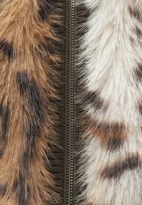 Kurtka z futra sztucznego w mieszance brązowych i kremowych tekstur, z centralnym metalowym zamkiem błyskawicznym i wyraźnymi wzorami przypominającymi zwierzęce.