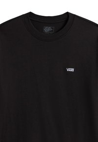 T-shirt noir ample avec petit logo Vans blanc sur la poitrine gauche et col rond.