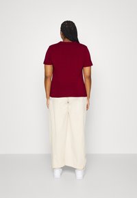 Maglietta a maniche corte bordeaux abbinata a pantaloni a gamba larga color crema. La maglietta presenta un classico colletto a girocollo; i pantaloni hanno un elastico all'orlo.