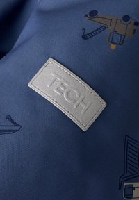 Tela azul marino con etiqueta en relieve gris "TECH". Presenta diseños ilustrados de herramientas y maquinaria en tonos más oscuros. Superficie texturada.