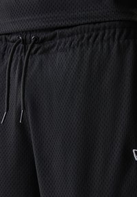 Black athletic shorts made of breathable mesh fabric, featuring an elastic waistband with drawstring and small white logo detail.
