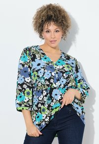 Blomstrete bluse med sort baggrund, prydet med store blå, grønne og hvide blomster. V-hals og 3/4 ærmer. Kombineret med mørke jeans.