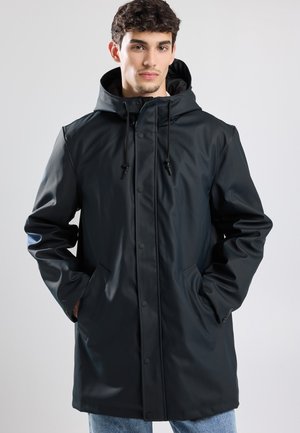 Parka waterproof noire avec capuche, dotée d'une fermeture à boutons-pression, d'un cordon de serrage et de deux poches latérales. Texture douce et lisse.