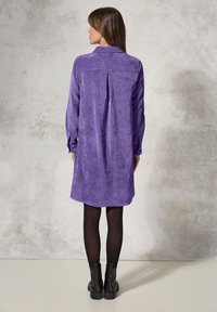 Paarse corduroy jurk met lange mouwen, een rugplooien en een zoom boven de knieën, gecombineerd met zwarte enkellaarsjes.