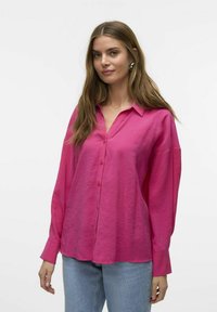 Lyserød langærmet skjorte med knaplukning, krave, afslappet pasform og blød tekstur. Vist sammen med lyseblå jeans og minimale accessories.