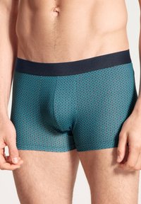 Heren boxershorts in donkerblauw met een geometrisch patroon in teal. Voorzien van een effen marineblauwe tailleband en een aansluitende, gladde textuur.