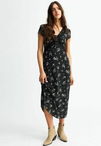 Abito midi nero con maniche corte, stampa floreale e scollo a V, caratterizzato da un dettaglio con coulisse e alte fessure laterali, abbinato a stivaletti beige.