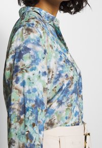 Floral-patterned shirt in blues and greens, featuring a collar, long sleeves, and a soft texture. Paired with a light-colored belt.