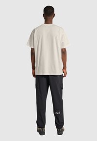 Lys beige oversized t-shirt med korte ærmer, parret med mørke cargo-bukser med sidelommer og hvid tekstdetalje.