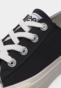 Κοντινό πλάνο μαύρου αθλητικού παπουτσιού με λευκά παχιά κορδόνια, μεταλλικά ρητίνια με τη στάμπα "Lee 1889" και λευκή σόλα πλατφόρμας.