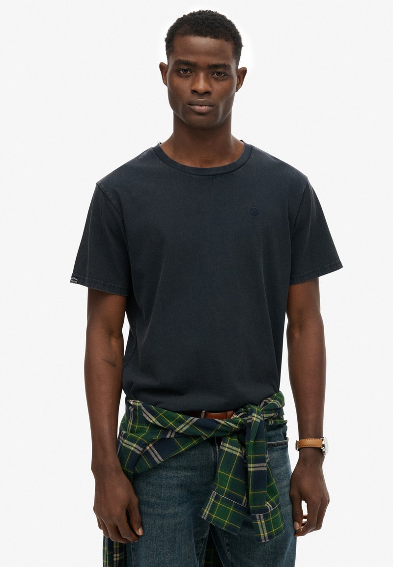 Mørkeblå bomulds t-shirt, rund hals, korte ærmer, parret med mørke denim jeans og en grønternet flannel skjorte knyttet om livet.