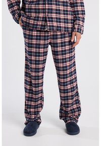 Plaid flannel pajama set in navy, red, and white. Loose-fitting top with buttons, matching pants, and soft navy slippers.