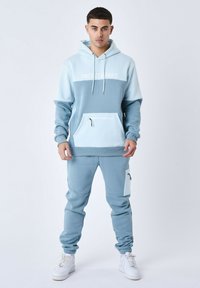 Conjunto de sudadera con capucha y pantalones de chándal en azul claro, con un diseño de bloques de color, bolsillo frontal con cremallera y puños acanalados.